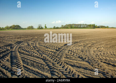 Le tracce delle ruote del trattore sul campo arato, orizzonte e cielo blu Foto Stock