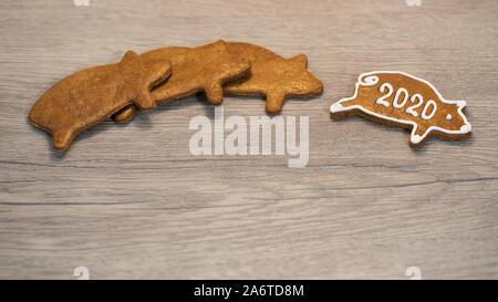 Nuovo anno 2020. Dolce a forma di maiale gingerbread cookie per buona fortuna. Carino golden piggies. Profumati dolci di Natale decorato con glassa bianca su sfondo di legno. Foto Stock