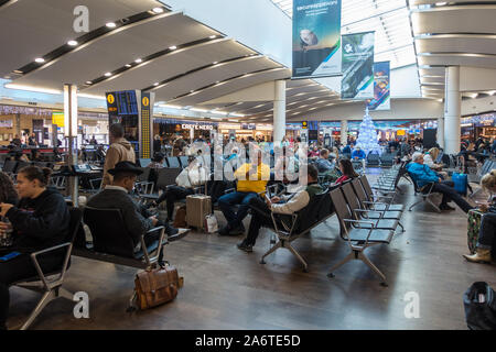 Persone sedersi e aspettare per i loro voli nella sala partenze dell'aeroporto di Heathrow Terminal 3. Foto Stock