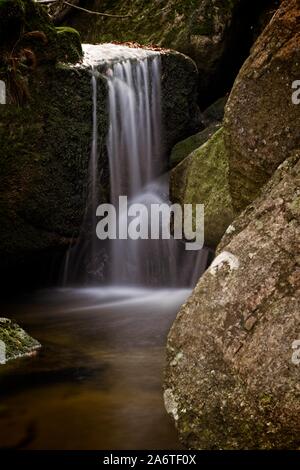 Autunno lunga esposizione del Creek e nero (grande) Stolpich cascate in Jizera Mountain. L'acqua cade in un profondo canyon di foresta piena di pietre di granito Foto Stock