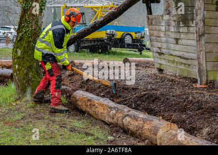 Registratori di giovani a lavorare con un'ascia su un parco giochi, dopo il taglio di tronchi di alberi con seghe a catena nel giorno di pioggia. Foto Stock