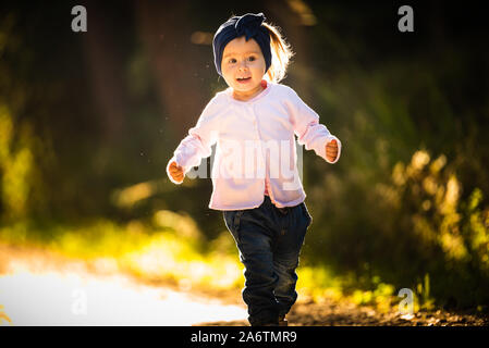 2 anni bambina in esecuzione nella foresta verso la telecamera. Con felice espressione sul viso Foto Stock