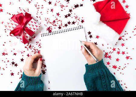 La donna a maglione verde scrive checklist dei piani e sogni per il prossimo anno. La lista dei desideri per il Natale e il nuovo anno. Per fare la lista per il nuovo anno 2020 con rosso Foto Stock