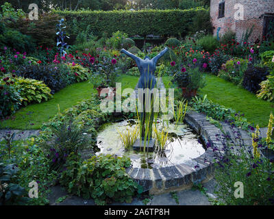 Bassa serata estiva sun causando un pool di luce su Chenies Manor Sunken Garden stagno ornamentale; in primo piano la scultura di raggiungere attraverso il dalie. Foto Stock