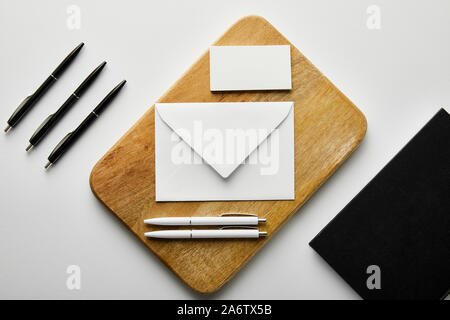Vista superiore della busta, business card e penne bianche sulla tavola di legno, notebook e penne nere sul tavolo Foto Stock