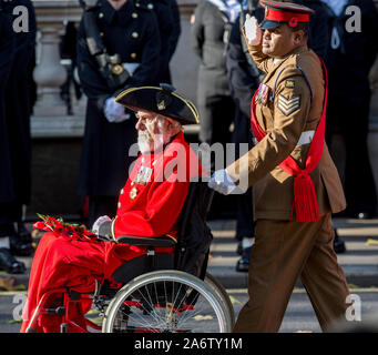 Victoria Cross destinatari William Speakman (Chelsea titolare di pensione o di rendita) essendo spinto nella sua sedia a rotelle dal compagno di destinatario Johnson Beharry, marching passato di Sua Maestà la Regina e il Duca di Edimburgo con altri membri della famiglia reale britannica che si unì a unire i leader politici e i membri del pubblico per ricordo un intervento di assistenza presso un serto cerimonia di posa presso il cenotafio in Whitehall, Londra, Inghilterra. Novembre 2017. Foto Stock