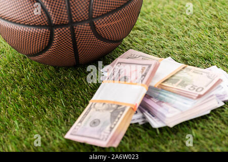 Vista ravvicinata del basket ball vicino a Dollar e le banconote in euro sulla verde erba, scommesse sportive concept Foto Stock