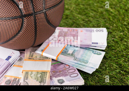 Vista ravvicinata del basket ball vicino a Dollar e le banconote in euro sulla verde erba, scommesse sportive concept Foto Stock