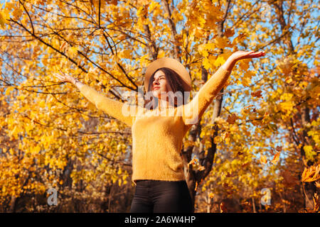 Caduta stagione attività. Donna gettando le foglie in autunno foresta al tramonto. Giovane donna avendo divertimento all'aperto godendo la natura Foto Stock