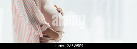 Panoramica della donna incinta in camicia a righe toccando ventre Foto Stock