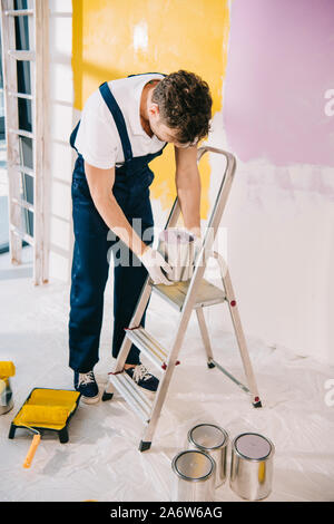 Giovane pittore in uniforme in piedi vicino alla scaletta e apertura può con vernice Foto Stock