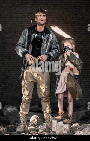 Uomo bello azienda pallone vicino a kid in maschera a gas, post concetto apocalittico Foto Stock