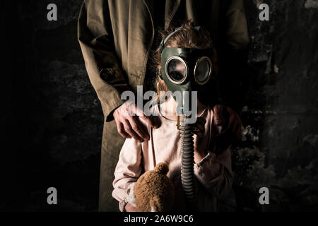 Vista ritagliata dell uomo in piedi vicino a kid in maschera a gas, post concetto apocalittico Foto Stock