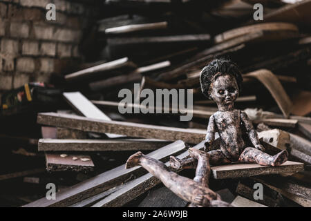 Bruciato e scary baby doll vicino danneggiato giocattolo e tavole di legno, post concetto apocalittico Foto Stock