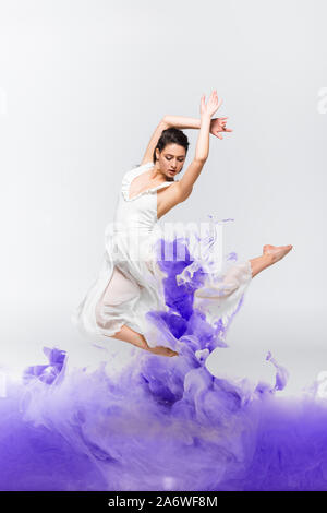 Bellissima ballerina in abito bianco dancing nei pressi di vernice blu schizzi sul dorso grigio terreno Foto Stock