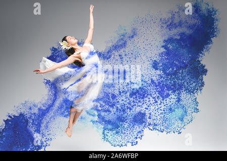 Giovane ballerina in abito bianco dancing in blu gli spruzzi di vernice su sfondo grigio Foto Stock