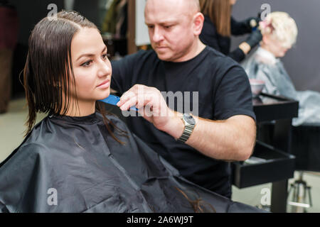 Hair stylist è rendere nuova acconciatura per la bella giovane donna nel salone di parrucchiere. Foto Stock