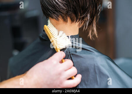 Mano di hair stylist è lo scuotimento cuted capelli con la spazzola dal collo della femmina nel salone di parrucchiere. Foto Stock