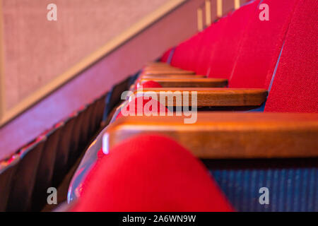 Una fila di sedili rosso, tipico di un teatro o un auditorium pubblico, viene osservato da vicino dal lato, mostrando i braccioli in legno e tessuto rosso cushioni Foto Stock
