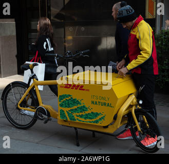 DHL lavoratore visto sul London High Street offrendo post su un motore elettrico bici di consegna. Foto Stock