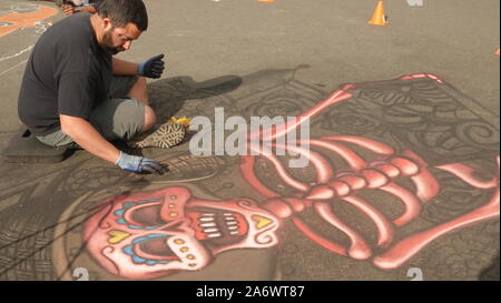 Chalk artista creazione di zucchero murale del cranio sulla strada durante un giorno dei morti evento. Foto Stock