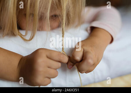 Carino bionda bambina in pigiama giocando nel letto bianco, la mattina presto prima di andare a scuola. Di coricarsi, playtime, concetto di rilassamento Foto Stock