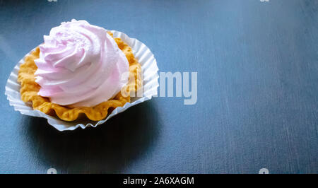 Delicato dessert, un cestello con crema leggera di luce rosa di meringa su una piastra bianca sul legno scuro dello sfondo. Foto Stock