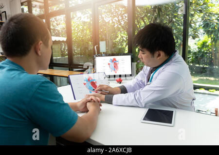 Medico paziente consultazione circa la cardiologia con spiegare il modello di un cuore su appunti in ufficio medico all'ospedale Foto Stock