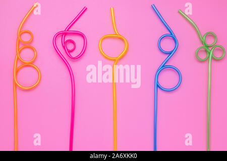 A spirale in plastica tubi multicolore su carta rosa card. Abstract sfondo colorato di forma curva cocktail cannucce. Design laconico. Concetto di divertimento dell'umore. Foto Stock