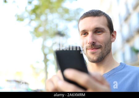 Close up di un uomo soddisfatto utilizzando smart phone a piedi in strada Foto Stock