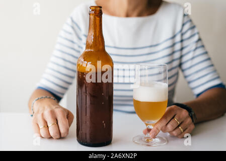 Donna seduta su un tavolo con un bicchiere di birra e una bottiglia. Foto Stock