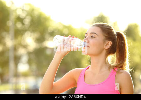 Happy runner acqua potabile da una bottiglia in piedi in un parco dopo lo sport Foto Stock