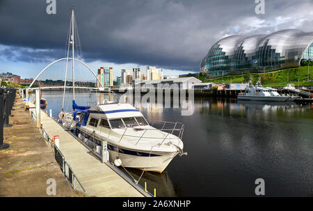 Un primo piano di uno yacht ormeggiati a Newcastle Quayside sul fiume Tyne con il Mar Baltico Art Museum, Sage Gateshead e Millennium Bridge a distanza Foto Stock