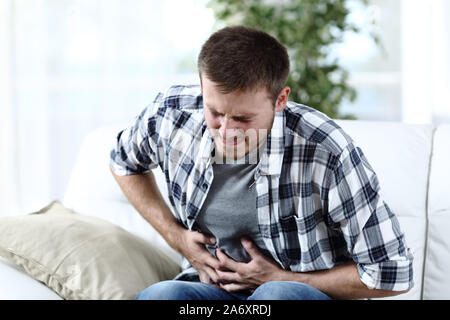 Casual Uomo seduto su un divano a casa lamentando la sofferenza mal di pancia Foto Stock