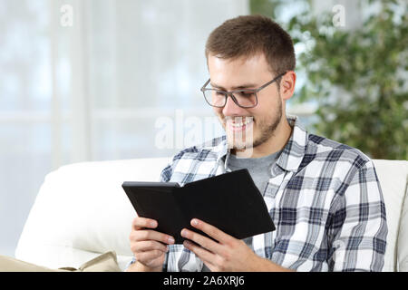 Uomo che indossa occhiali di lettura di un ebook seduta su un divano nel salotto di casa Foto Stock