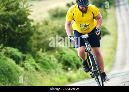 ROTHBURY, NEWCASTLE UPON TYNE, Regno Unito - Luglio 06, 2019: un giovane ciclista in un giallo brillante t-shirt peddling disco fino alla cima di una collina a ciclone vigilia di gara Foto Stock