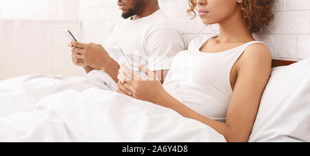 Coppia africana nel litigio, utilizzando i telefoni cellulari nel letto Foto Stock