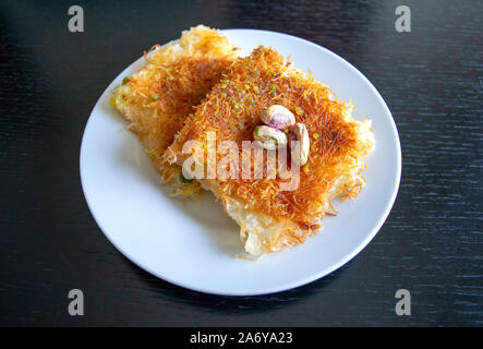 Tradizionale orientale kunafa dessert. Vista dall'alto. Formaggio arabo kunafa nella piastra bianca sul legno scuro tavolo. Konafa. Foto Stock