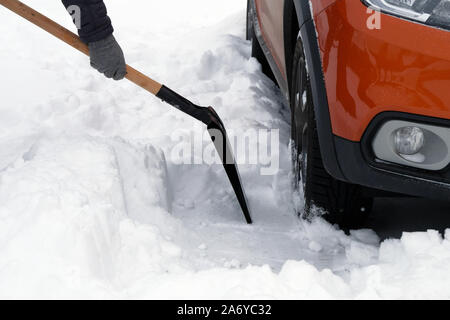 Uomo con la pala si cancella la neve intorno auto nel parcheggio in inverno dopo la nevicata. Pala in mano. Problemi invernali di automobilisti. Foto Stock