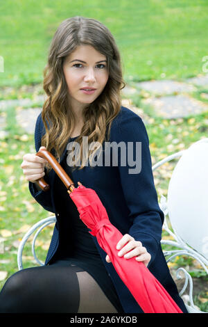 Ragazza con un ombrello rosso nelle sue mani su una panchina nel parco Foto Stock