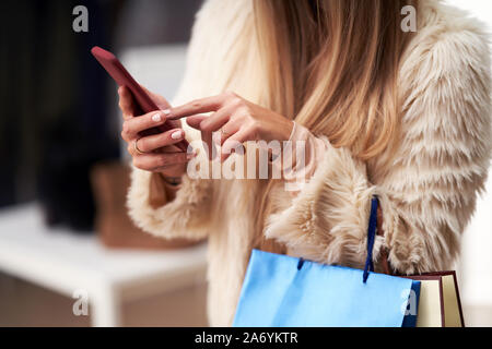 Le donne in età adulta shopping per i vestiti in boutique in autunno e utilizza lo smartphone Foto Stock