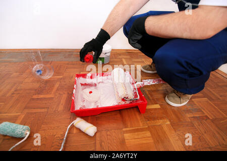 Operaio edile finitura facendo lavori di rinnovo nell'appartamento. Pittore con guanti neri rosso versa il pigmento di colore per la verniciatura di parete della camera dalla bottiglia. Foto Stock