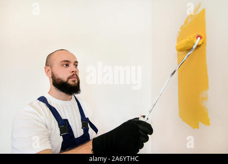 Lavoratore edile e tuttofare finitura facendo lavori di rinnovo nell'appartamento. Pittore utilizzando una vernice spazzola a rullo la pittura della parete con il colore giallo. Foto Stock