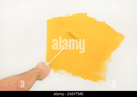 Lavoratore edile e tuttofare finitura facendo lavori di rinnovo nell'appartamento. Pittore utilizzando una vernice spazzola a rullo la pittura della parete con il colore giallo. Foto Stock