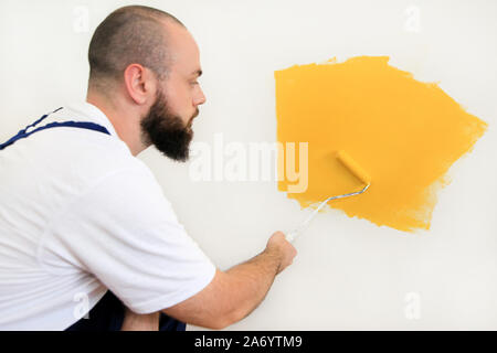 Lavoratore edile e tuttofare finitura facendo lavori di rinnovo nell'appartamento. Pittore utilizzando una vernice spazzola a rullo la pittura della parete con il colore giallo. Foto Stock
