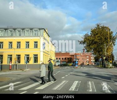 Una coppia di anziani su un attraversamento pedonale davanti di un giallo brillante hotel in Ystad, Svezia. Foto Stock