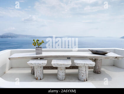 Terrazzo al fresco aria aperta robusta strong White wash tavolo da pranzo plank sedie sgabelli vista verso le montagne di fronte mare Mediterraneo acqua in Oia Santorini Foto Stock