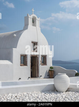 Un bucato bianco chiesa cappella porta aperta piccola torre campanaria con cross cruicifix blue sky cloud pot ciottoli bassa parete primo piano Oia Santorini Foto Stock