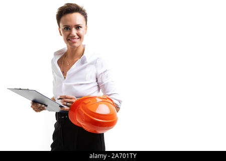 Bruna tecnico su uno sfondo bianco con un casco arancione sul gomito guarda la telecamera con un sorriso Foto Stock