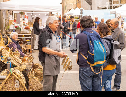 Un maschio di cestello tessitore a un mercato di artigianato in una cittadina collinare in Italia a parlare con alcuni clienti Foto Stock